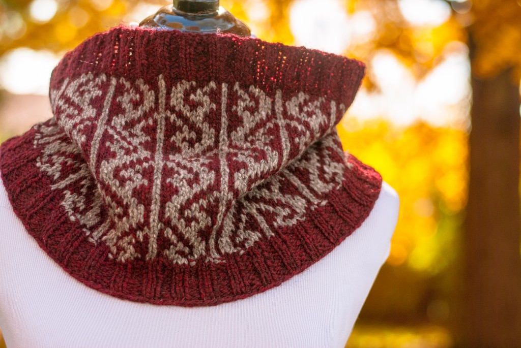 a red and taupe cowl with stranded colorwork on a dressform in front of golden autumn leaves