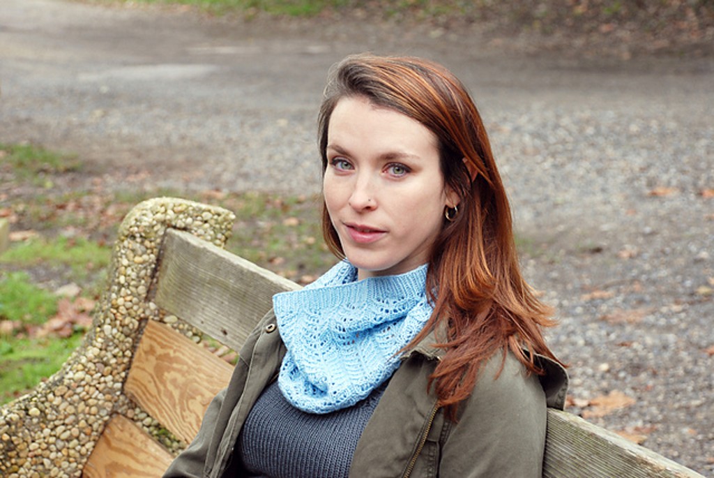 a woman sits on a bench wearing a lacy blue cowl
