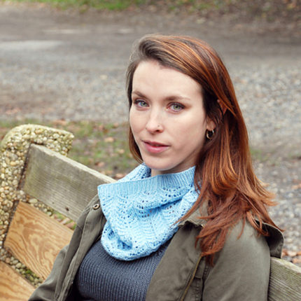 a woman sits on a bench wearing a lacy blue cowl
